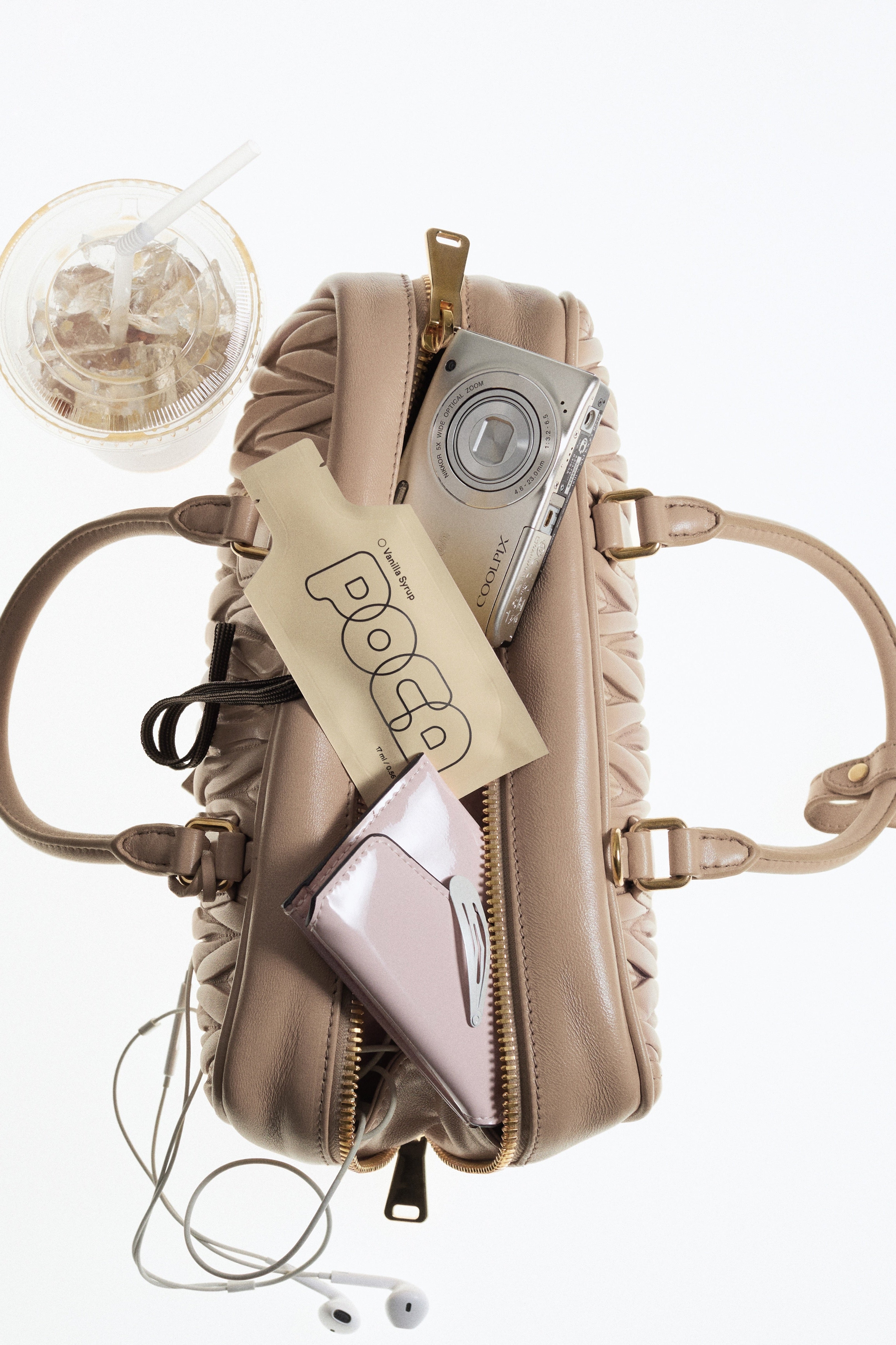 Beige handbag with a camera, phone, and Vanilla POCA inside of it.