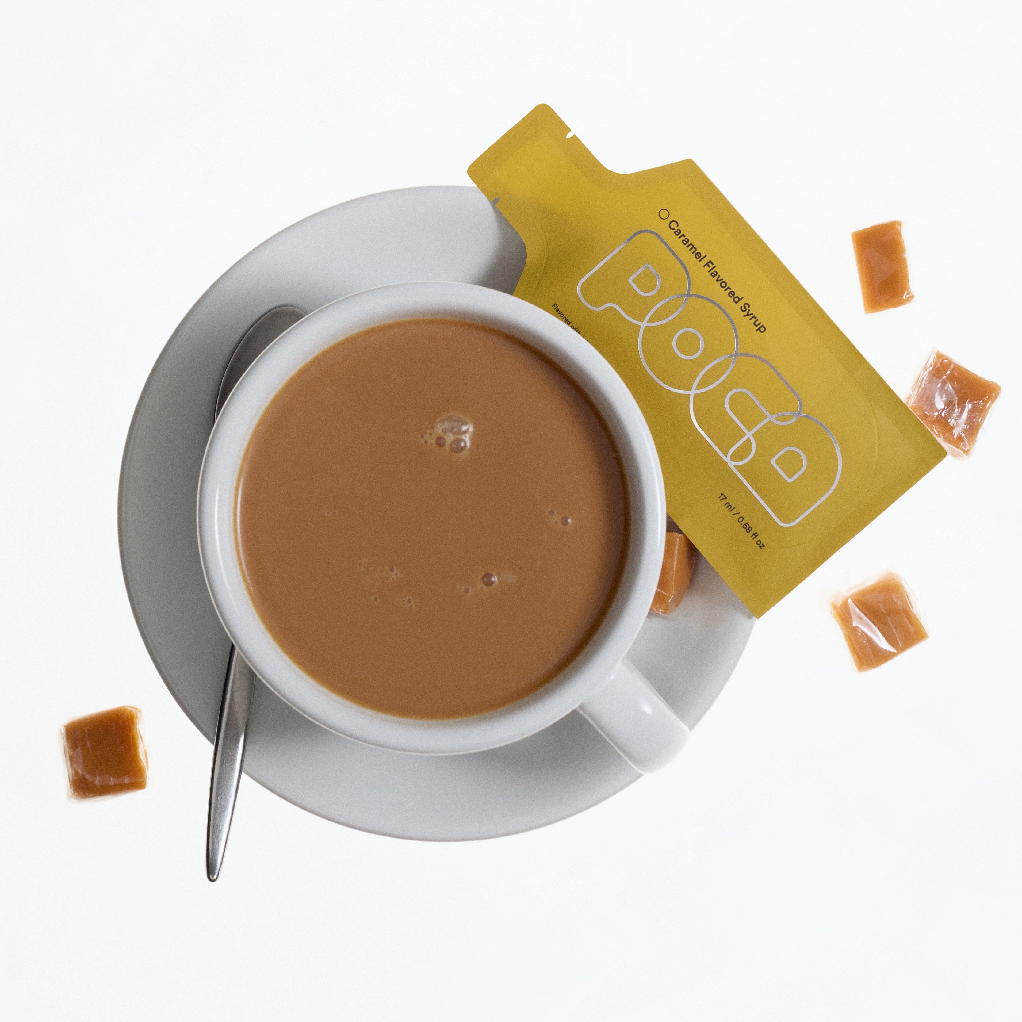 Cup of coffee with a spoon and a yellow packets labeled POCA Caramel Flavored Syrup. 